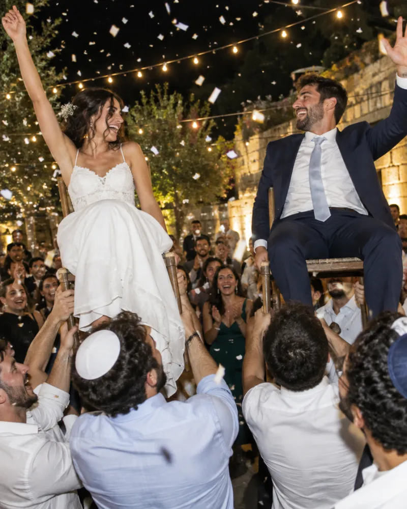 רחבת ריקודים בחתונה: האורחים מרימים את הזוג על כיסאות בתוך ענן קונפטי
